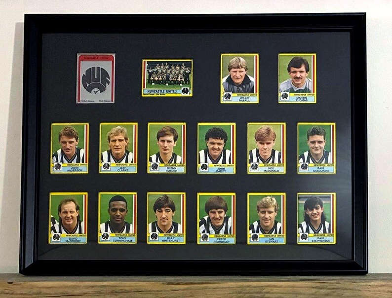 May include: A black framed display featuring a collection of vintage Newcastle United football trading cards. The arrangement includes a team logo card, a team photo, and individual player portraits with names printed below each image.