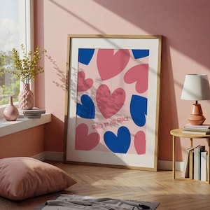 May include: A framed art print with a pattern of pink and blue hearts on a pale pink backdrop. The text "SAVED BY HIS GRACE" is printed in a red-orange colour at the bottom. The frame is a light wood colour.