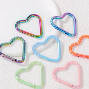 May include: A collection of heart-shaped carabiner clips in various iridescent colors, including rainbow, blue, green, and pink. These decorative clips have a spring-loaded gate for secure attachment.