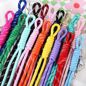 Pode incluir: Uma coleção de cordões de paracord multicoloridos com um design de alça trançada. Os cordões estão disponíveis em várias cores sólidas, incluindo azul, verde, rosa, laranja, amarelo, roxo, vermelho e preto, com um fio branco refletivo.