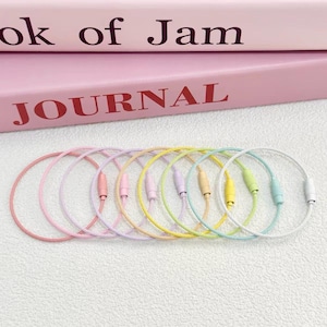 May include: A set of eight circular wire cable keychains in pastel colors including pink, yellow, lavender, mint, and white. Each keychain features a threaded metal screw-lock barrel closure. The cables are arranged in a row.