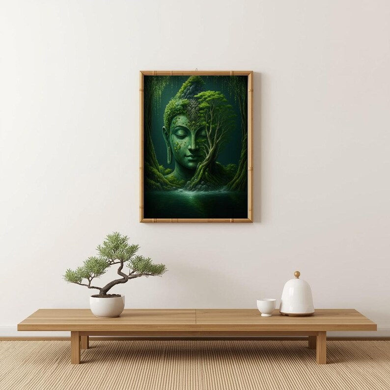 A framed print of a green Buddha head in a forest, with trees growing on its head and face, displayed on a light wooden table with a small bonsai tree.