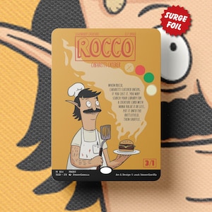 May include: A trading card featuring a cartoon chef with a mustache holding a burger. The card has the name "Rocco" and the text "Surge Foil". The card's background is tan with a cartoon face.