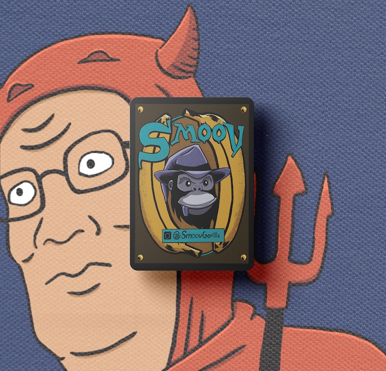 Puede incluir: Un pin rectangular con un gorila de dibujos animados con un sombrero fedora, sobre un fondo dorado y marr&oacute;n. El pin tiene la palabra "Smoov" en verde azulado y el identificador de Instagram "@SmoovGorilla". El fondo es de tela azul.