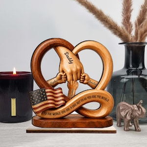 May include: A wooden sculpture in the shape of a pretzel, featuring the words "Daddy", "Sophia", "Amelia", and "Thomas". An American flag is included. The text reads "TO THE WORLD, YOU ARE A DAD, BUT TO US, YOU ARE THE WORLD".