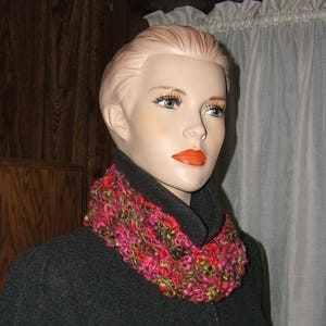 May include: A mannequin wearing a gray coat with a pink, green, and brown crocheted scarf.