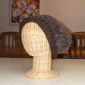 May include: A brown knitted hat with a fuzzy texture on a wicker mannequin head.