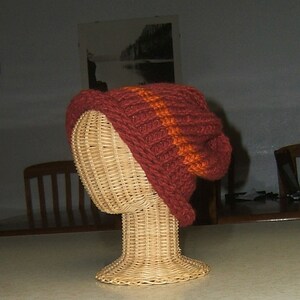 May include: A brown knitted hat with orange stripes on a wicker hat form.
