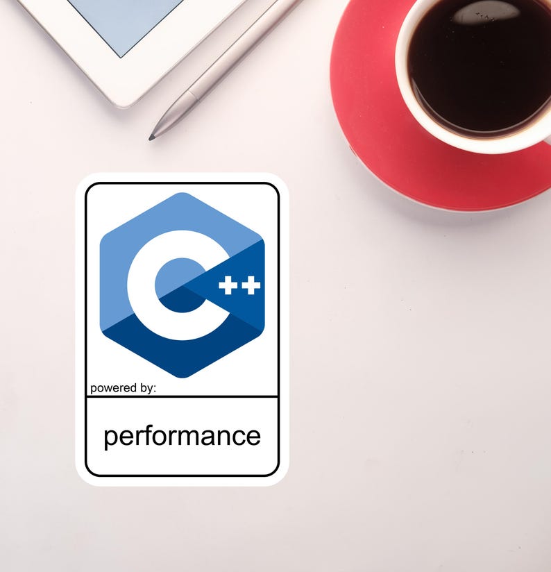 May include: A sticker with the C++ programming language logo, a blue hexagon with a white "C" and "++" symbols. The text "powered by: performance" is below the logo. A cup of coffee and a tablet are also visible.