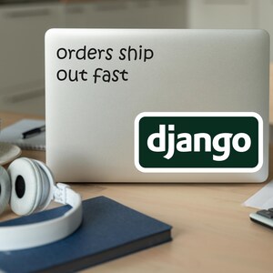 Może przedstawiać: Laptop z naklejką z napisem "orders ship out fast" i naklejką Django. Białe słuchawki, niebieski notatnik, filiżanka i kalkulator leżą na drewnianym biurku.