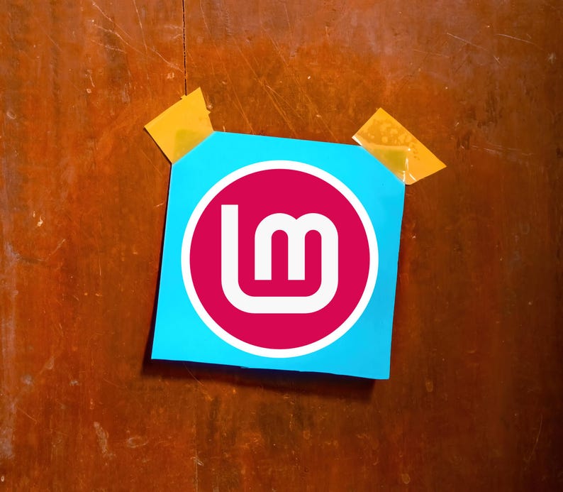May include: A blue square sticker with a white and magenta logo, taped to a wooden surface with two pieces of yellow tape. The logo features the letters "lm" in white within a magenta circle.