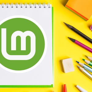 May include: A white spiral-bound notebook with a green border and a green circle logo with the letters "Lm" is on a yellow surface. Pencils, an eraser, and a pencil sharpener are also on the surface.