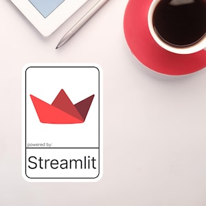 K&ouml;nnte beinhalten: Ein wei&szlig;er Aufkleber mit einem roten Papierboot-Logo und dem Text "Streamlit". Der Aufkleber befindet sich auf einer wei&szlig;en Oberfl&auml;che, neben einem Tablet, einem Stift und einer Tasse Kaffee auf einer roten Untertasse.