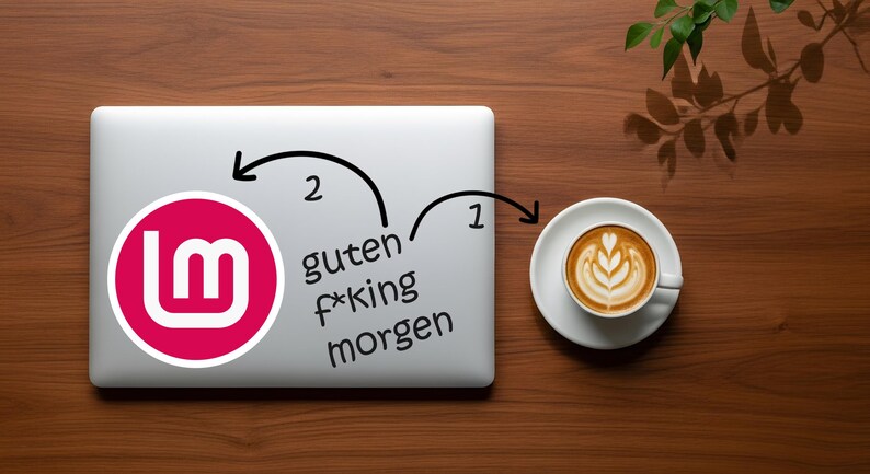 May include: A laptop with a pink and white logo sticker and the German phrase "guten f*king morgen" is next to a cup of coffee with latte art on a wooden surface.
