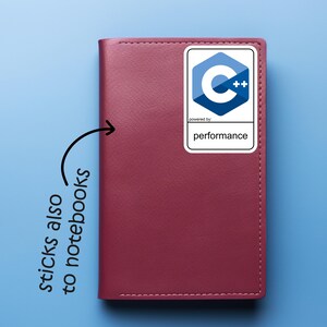 May include: A burgundy notebook with a white sticker featuring a blue and white C++ logo and the word "performance". The sticker is on the upper right corner of the notebook. The text "sticks also to notebooks" is written on the left side of the notebook.