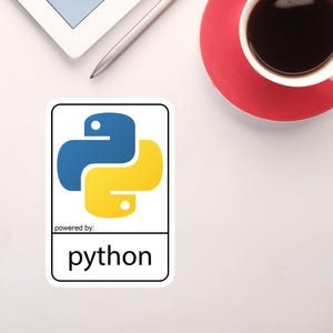 May include: A white sticker with the Python logo, featuring a blue and yellow snake-like design. The text "powered by: python" is below the logo. A cup of coffee on a red saucer and a tablet with a stylus are in the background.