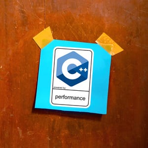 May include: A cyan sticky note featuring a white and blue C++ logo and the word "performance" printed below. The note is affixed to a wooden surface with two pieces of yellow tape.