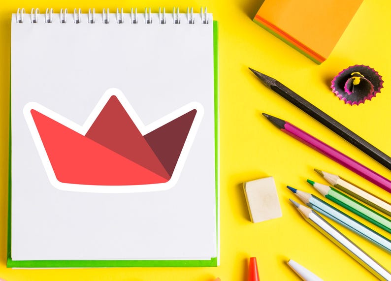 Op de afbeelding: Een witte notitieblok met een rode papieren kroonsticker. De afbeelding bevat ook potloden, een gum en een puntenslijper op een gele achtergrond. Kantoorartikelen voor school of kantoor.