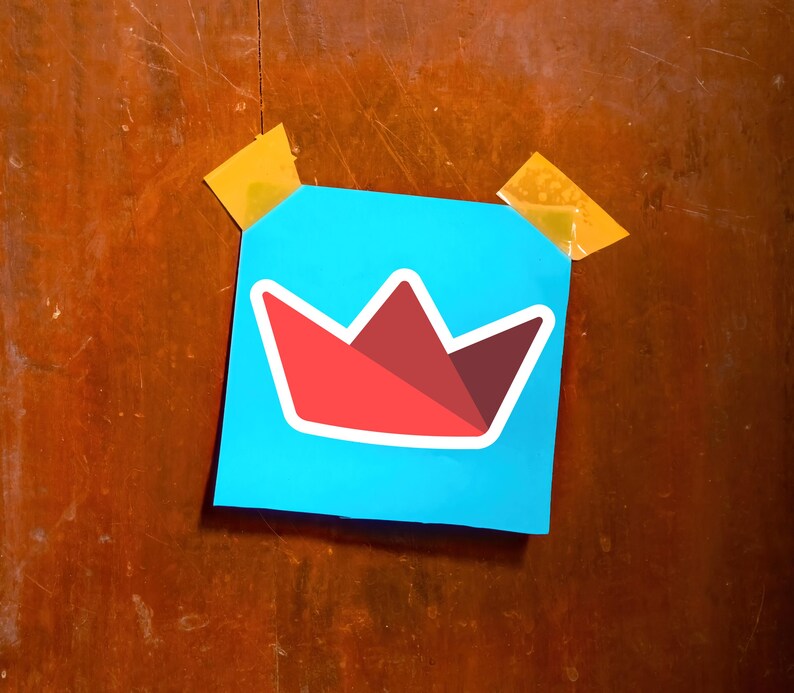 Op de afbeelding: Een vierkante, lichtblauwe post-it met een rood-wit kroonontwerp, bevestigd op een houten oppervlak met twee stukjes gele tape. De kroon heeft een geometrische vorm.