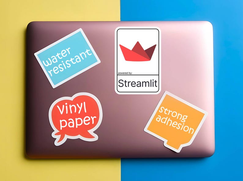 K&ouml;nnte beinhalten: Auf einem Laptop befinden sich mehrere Aufkleber. Die Aufkleber zeigen die Texte "water resistant", "vinyl paper" und "strong adhesion". Ein Aufkleber zeigt ein rotes Origami-Boot-Design mit dem Text "powered by: Streamlit".
