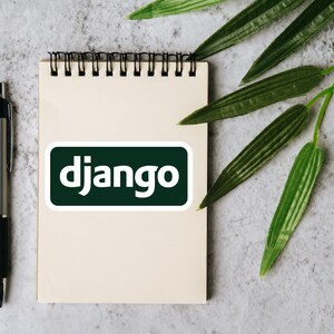 Może przedstawiać: Notatnik ze spiralą, długopis i naklejka z napisem "django" białymi literami na ciemnozielonym tle. Zielone liście w tle. Długopis jest srebrny i czarny.