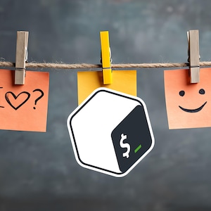 May include: A decorative arrangement featuring three sticky notes suspended by clothespins on a string. The notes display the phrases "I ♡?" and a smiley face, with a cube-shaped logo in the center. The background is a textured gray.