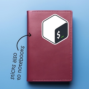May include: A burgundy notebook with a white and black sticker featuring a dollar sign and a green underscore. The sticker is in the shape of a hexagon. Text on the image says "sticks also to notebooks". The notebook is on a blue background.