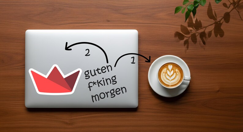 Op de afbeelding: Een laptop met een rood-witte kroonsticker en de Duitse zin "guten f*king morgen" staat naast een kop koffie met latte art op een houten oppervlak. Een takje bladeren bevindt zich in de rechterbovenhoek.