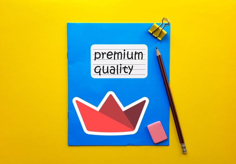Op de afbeelding: Een blauw notitieboek met de woorden "premium quality" op een witte sticker. Een rode en witte papieren kroonsticker staat onder de tekst. Een potlood, gum en een gele paperclip liggen ook op de gele achtergrond.