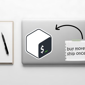 May include: A white and dark teal sticker with a dollar sign graphic is on a laptop. A notepad with the text "buy more, ship once" is taped to the laptop. A black pen and notepad are on the left.