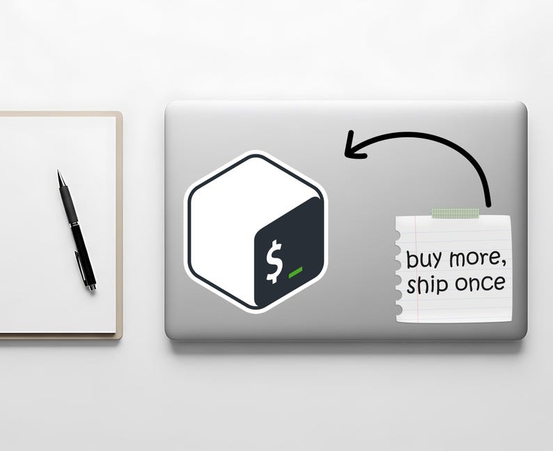May include: A white and dark teal sticker with a dollar sign graphic is on a laptop. A notepad with the text "buy more, ship once" is taped to the laptop. A black pen and notepad are on the left.