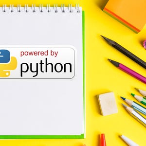 May include: A white spiral-bound notebook with a green border and the text "powered by python" on a white sticker. Pencils, an eraser, and a sharpener are scattered on a yellow surface.