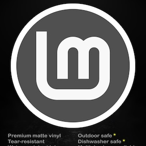 Puede incluir: Una pegatina circular con fondo gris y logotipo "lm" blanco. La pegatina tiene un borde blanco y el texto "stick me! somewhere cool..." en amarillo. Texto adicional indica que es vinilo mate de primera calidad, resistente al desgarro y al agua.