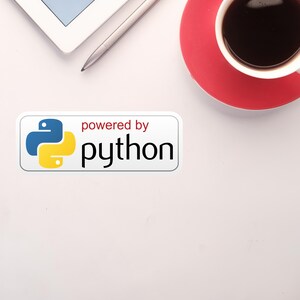 May include: Overhead shot of a white desk with a tablet, stylus, and a coffee cup on a red saucer. A sticker with the Python logo and the text "powered by python" is also visible.