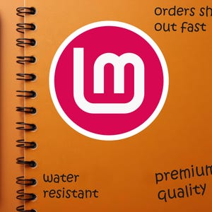 May include: An orange spiral-bound notebook with a black pen on the left side. A pink circle with white text is in the center. The notebook has the words "orders ship out fast", "water resistant", and "premium quality".