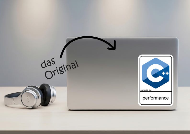 May include: A silver laptop with a sticker featuring a blue and white C++ logo and the text "performance." The words "das Original" are written in black. Silver headphones are on the table.