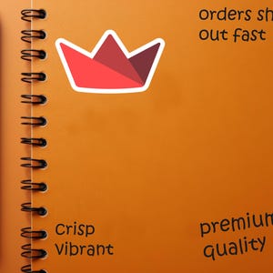 Op de afbeelding: Een oranje spiraalgebonden notitieboek met een zwarte pen aan de linkerkant. Een rode en witte kroonsticker staat in het midden. Tekst bevat "orders ship out fast", "Crisp Vibrant" en "premium quality".