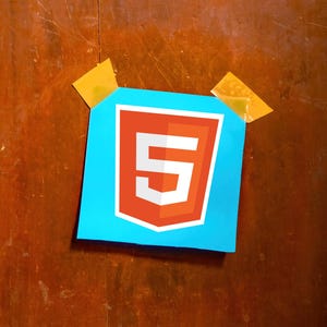 May include: A blue paper with the number 5 inside a red and white shield, taped to a wooden surface with two pieces of yellow tape. The number 5 is white and the shield is red with a white border.