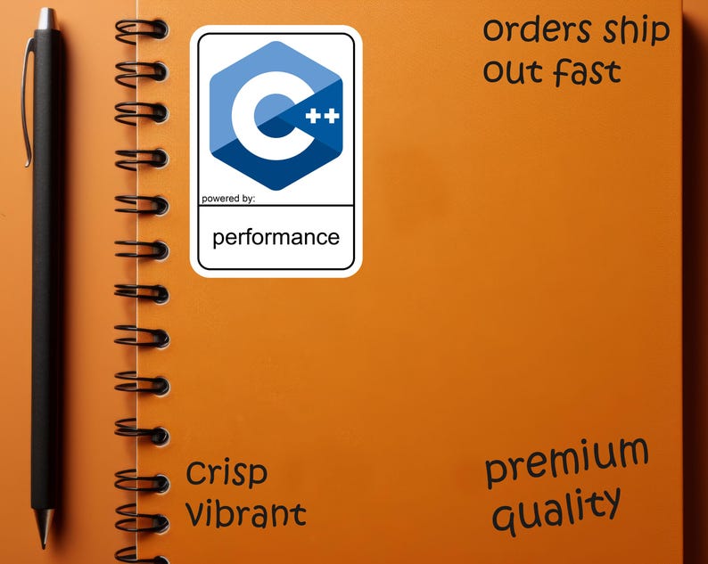 May include: An orange spiral-bound notebook with a black pen and a sticker featuring a blue and white C++ logo. The sticker reads "powered by: performance." Additional text includes "Crisp Vibrant" and "premium quality."