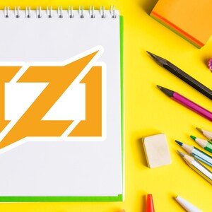 Puede incluir: Un cuaderno blanco con espiral, borde verde y logotipo naranja. L&aacute;pices, una goma de borrar y un sacapuntas est&aacute;n sobre una superficie amarilla brillante, creando un espacio de trabajo colorido.