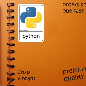 May include: An orange spiral notebook with a black pen and a Python sticker. The sticker features a blue and yellow logo with the word "python" below. The notebook has the words "Crisp Vibrant" and "premium quality".
