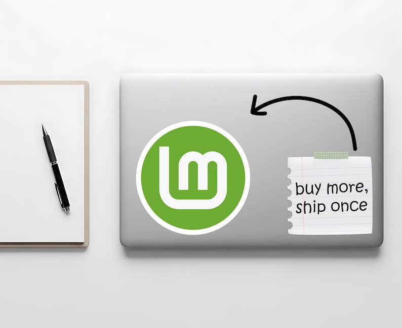 May include: A laptop with a green and white logo sticker and a sticky note that says "buy more, ship once". A black pen and a white notepad are on the left.