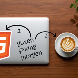 May include: A laptop with a sticker of the HTML5 logo and the text "guten f*king morgen". A cup of coffee with latte art sits to the right. The items are on a wooden surface.