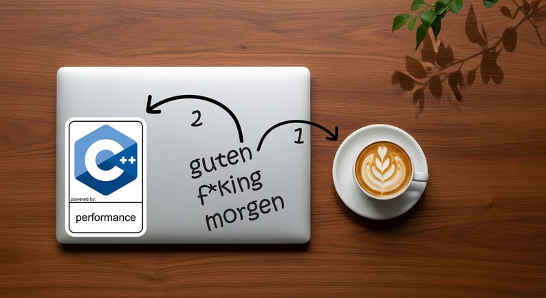 May include: A laptop with a C++ logo sticker and the words "guten f*king morgen" written on it. A cup of coffee with latte art sits to the right. The items are on a wooden surface.