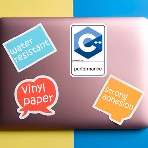 May include: A selection of stickers on a laptop. The stickers feature the text "water resistant", "Vinyl paper", "Strong adhesion", and a C++ logo with the word "performance". The laptop is pink and rests on a yellow and blue background.