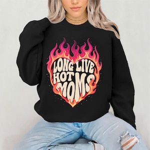 May include: Black sweatshirt with a heart-shaped graphic that reads "LONG LIVE HOT MOMS" in a retro font, surrounded by flames in shades of red, orange, and yellow. The sweatshirt is a crew neck style.