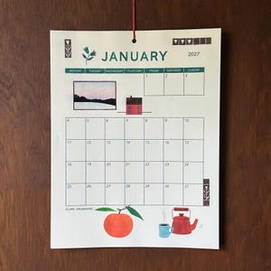 May include: A wall calendar for January 2027 featuring a grid layout with days of the week. The design includes a small illustration of a landscape, a red house, an orange fruit, and a red teapot with a blue mug. The text reads JANUARY 2027.