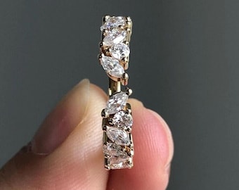May include: A gold-toned ring with a series of clear, marquise-cut and round-cut gemstones. The gemstones are set closely together, creating a continuous sparkle. The ring is held against a blurred, dark background.