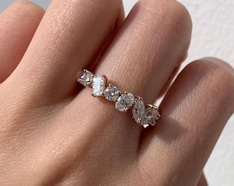 May include: A rose gold ring featuring a series of clear, sparkling gemstones in various shapes, including oval, marquise, and emerald cuts. The ring is set with multiple stones, creating a unique and eye-catching design.