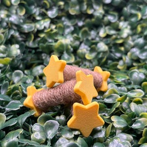 May include: A close-up of yellow star-shaped embellishments on a brown twine bundle, set against a backdrop of green foliage. The stars are evenly spaced and appear to be made of a solid material. The twine is tightly wound.